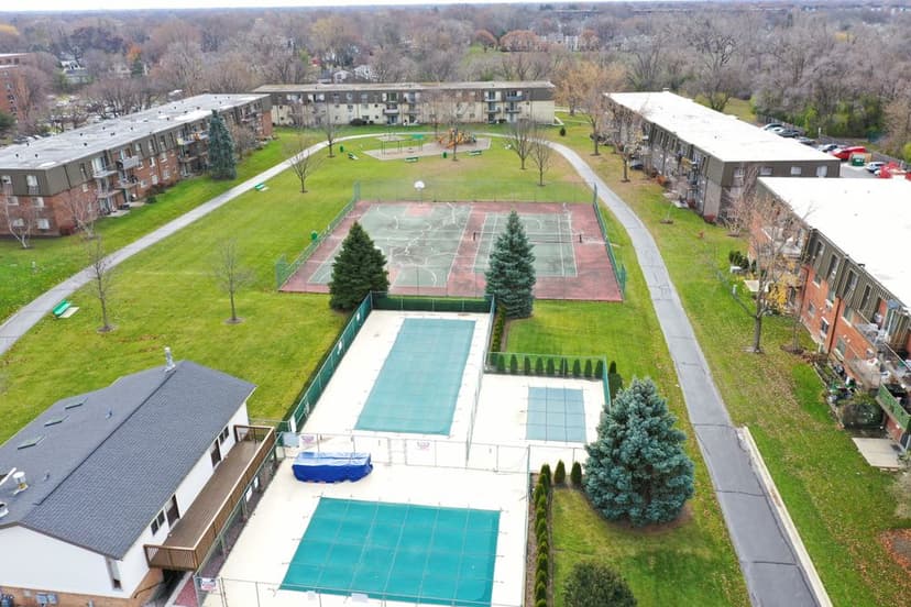 Aerial view of tennis courts and green space in a residential community with trees.